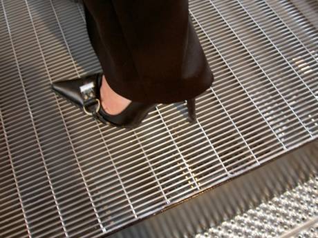 One foot wearing black high heel standing on dense steel grating without falling.