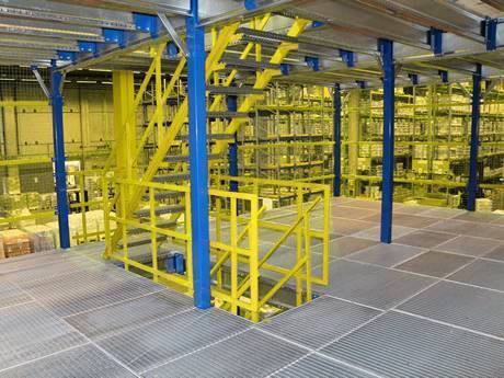 Dense steel grating used as mezzanine in a warehouse with many shelves.