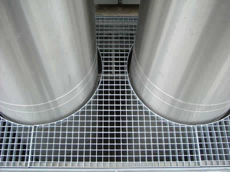 Two cylindrical pipes pass through the steel grating operating platform to the next floor.