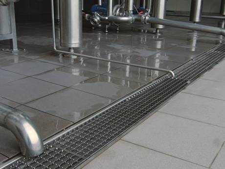 A serrated press-locked steel grating placed on the ground for drainage in a factory.