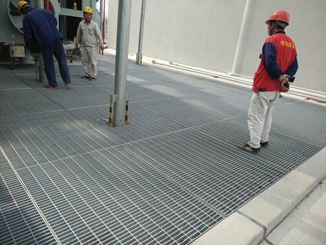 Three workers standing on steel grating floor are working.