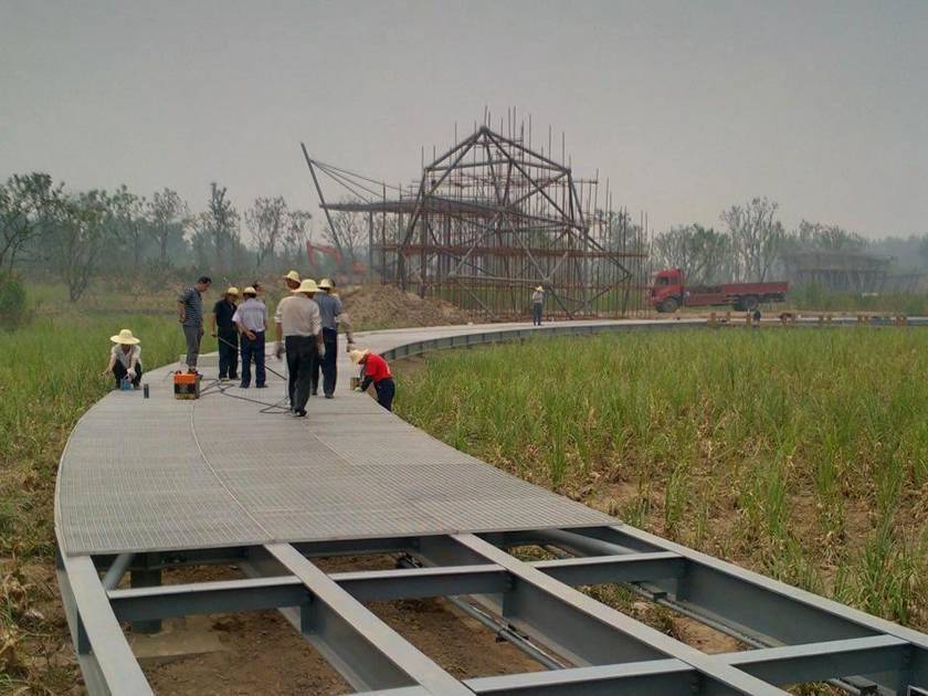 Several workers are installing the steel grating walkway in the fields.